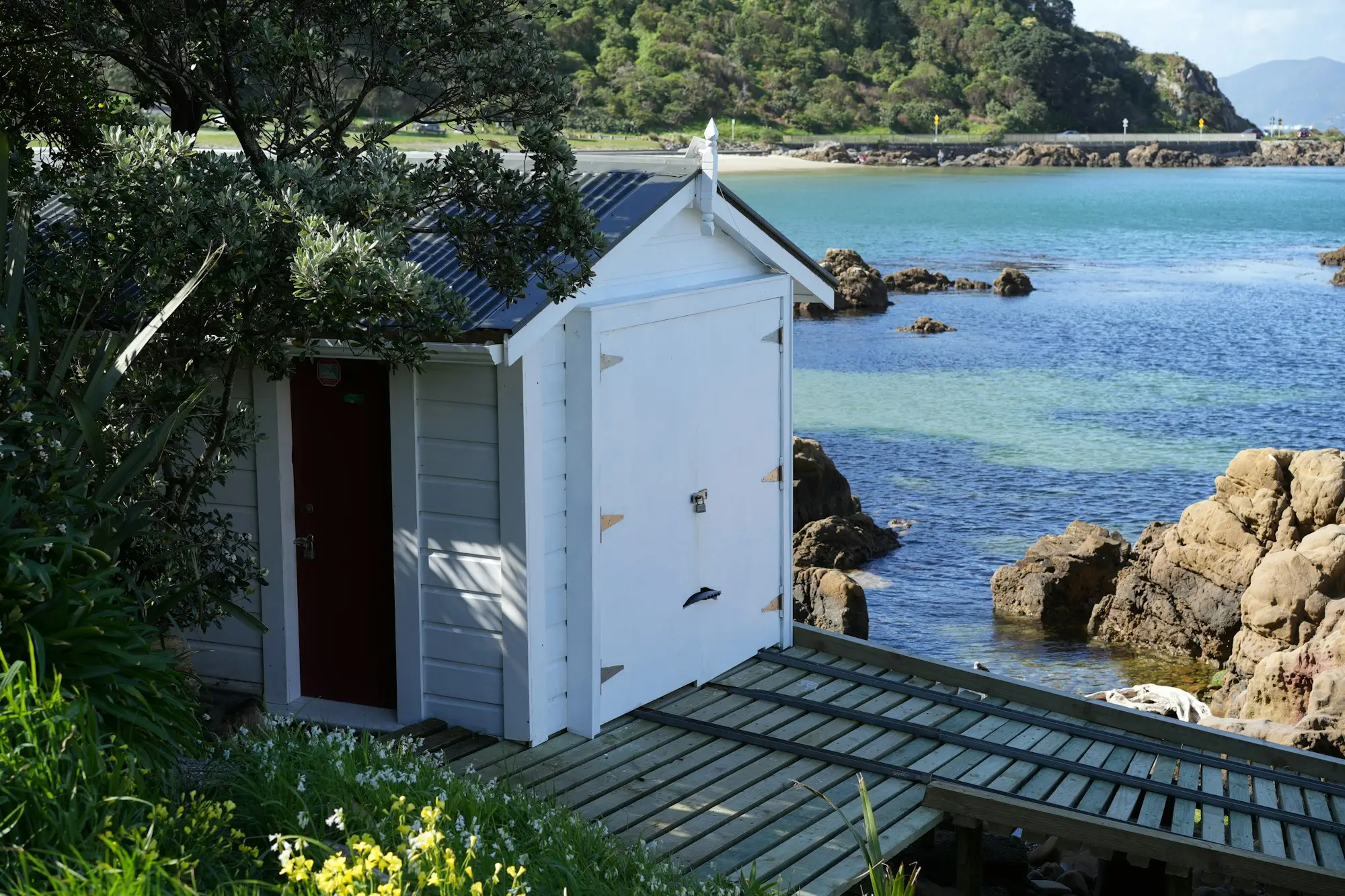 White timber boatshed beside a clear rocky bay in New Zealand summer, the season when lawyers and lenders close for the Christmas break