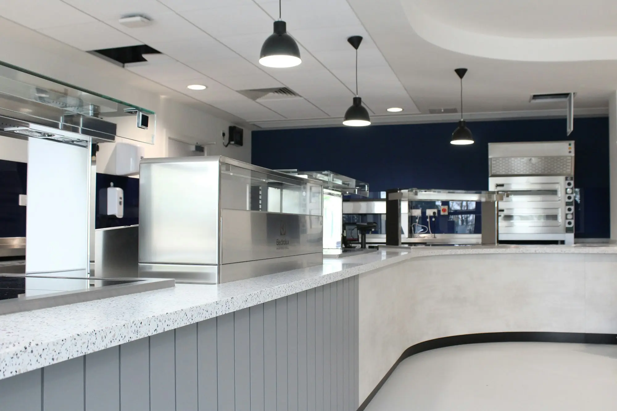 Empty commercial kitchen counter with stainless steel equipment and pendant lights in a small food business